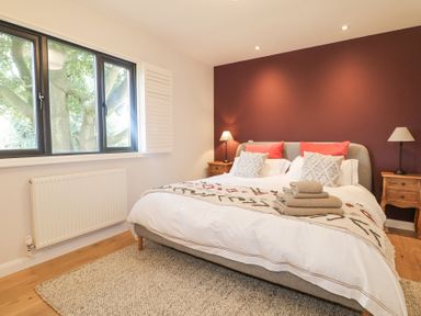 A bedroom with a double bed two bedside tables with lamps and a window showing a tree at Holm Oaks Cottage in Busbridge near Godalming