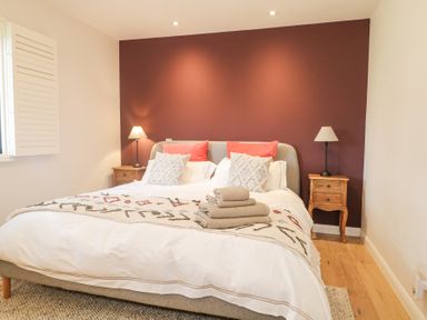 A bedroom with a bed between two wooden nightstands with lamps at Holm Oaks Cottage in Busbridge near Godalming