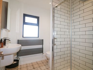 A bathroom with a sink, a window, a wall-mounted towel radiator, a toilet, and a glass shower enclosure with white subway tiles at Holm Oaks Cottage in Busbridge near Godalming