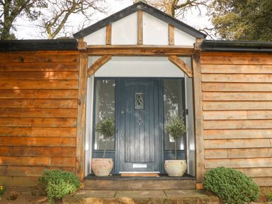 A wooden exterior entrance with a dark blue door and potted plants at Holm Oaks Cottage in Busbridge near Godalming