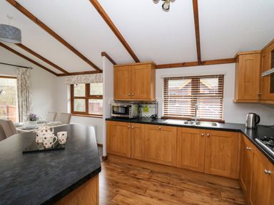A kitchen with wooden cabinets black countertops and a dining table with chairs at 2 Riverside Lodge Abercych near Cenarth