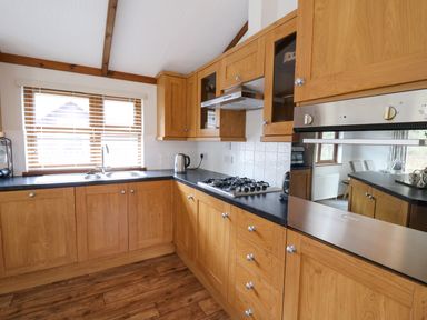 A kitchen with wooden cabinets a gas stove a sink under a window and a built in oven at 2 Riverside Lodge in Abercych near Cenarth