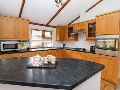 A kitchen with wooden cabinets black countertops a microwave a kettle a stove an oven and polka dot teapot set on the island at 2 Riverside Lodge Abercych near Cenarth
