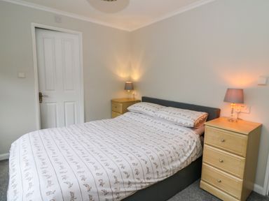 A bedroom with a double bed between two wooden bedside cabinets with lamps at 2 Riverside Lodge in Abercych near Cenarth