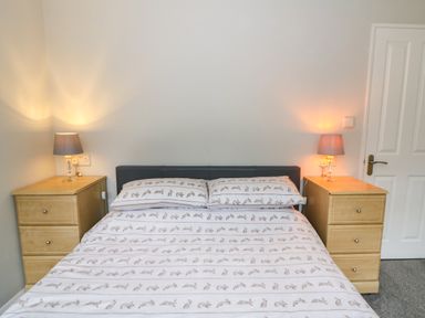 A bedroom with a bed in the center flanked by two wooden nightstands each with a lamp at 2 Riverside Lodge in Abercych near Cenarth