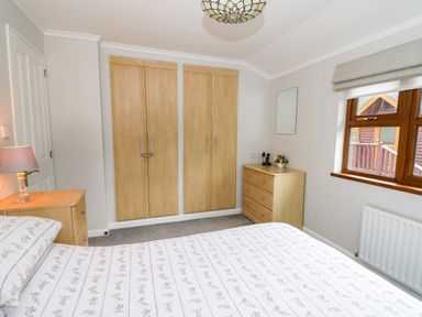 A bedroom with a bed covered with patterned sheets a wooden wardrobe a wooden chest of drawers and a window at 2 Riverside Lodge in Abercych near Cenarth