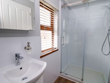 A bathroom with a sink, mirror, window with blinds and a glass shower enclosure at 2 Riverside Lodge Abercych near Cenarth