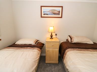 A bedroom with two single beds separated by a wooden nightstand with a lamp and a framed picture on the wall at 2 Riverside Lodge in Abercych near Cenarth