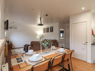 A dining table set with plates bowls glasses and candles next to a living room with brown sofas and animal pictures on the wall at Hub House in Three Oaks near Hastings