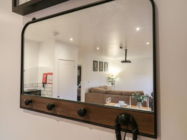 A wall mirror reflecting a living room with a brown sofa a dining table set with plates glasses and a vase with flowers at Hub House in Three Oaks near Hastings