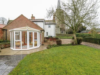 A garden with a conservatory and a church in the background at White Gates in Banham