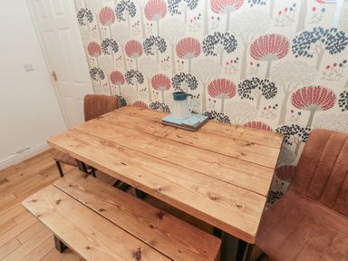 A wooden dining table with a bench and two chairs against a patterned wall at The Smithy in Chathill near Seahouses