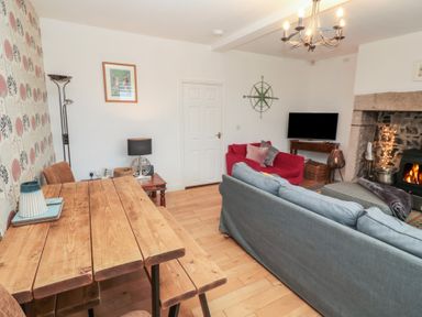 A living room with wooden dining table a blue sofa and a red armchair near a fireplace at The Smithy in Chathill near Seahouses