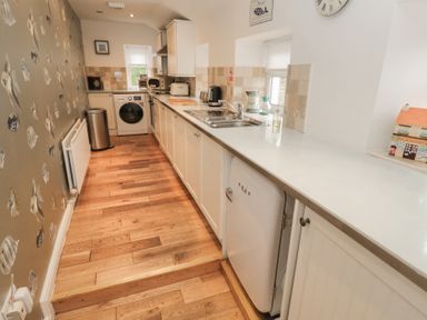 A kitchen with wooden floor white cabinets a sink appliances and fish wallpaper on one wall at The Smithy in Chathill near Seahouses