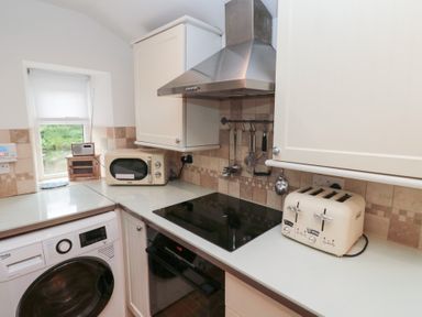 A kitchen corner with a washing machine a microwave a toaster an electric stove and cooking utensils hanging on the wall at The Smithy in Chathill near Seahouses