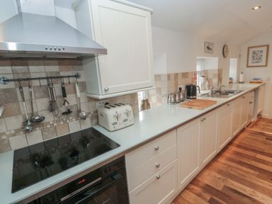 A kitchen with white cabinets a stovetop under a stainless steel hood and utensils hanging on the wall at The Smithy in Chathill near Seahouses