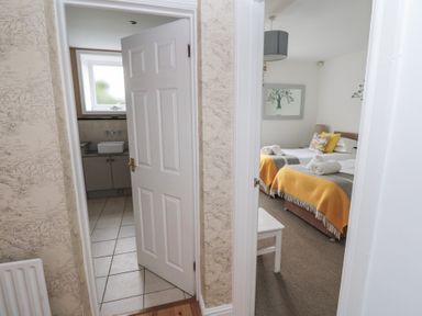 View of a bathroom with tiled floor and a bedroom with two beds covered with yellow and gray blankets at The Smithy in Chathill near Seahouses