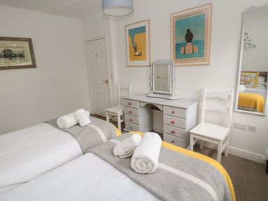 A bedroom with two single beds with white linens and gray blankets a white vanity desk with a mirror and two chairs at The Smithy in Chathill near Seahouses