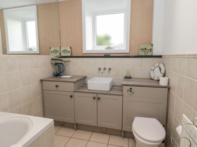 A bathroom with a bathtub toilet and sink with beige cabinets and a window above the sink at The Smithy in Chathill near Seahouses