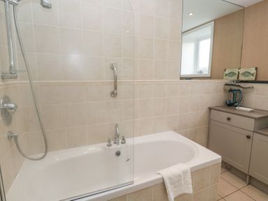 A bathroom with a bathtub fitted with a shower and a cabinet with decorative items at The Smithy in Chathill near Seahouses