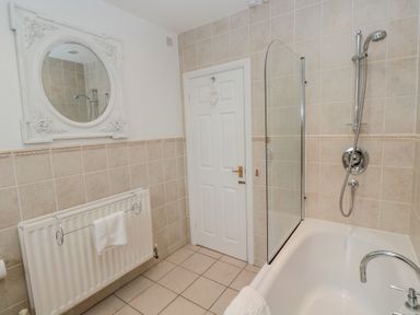 A bathroom with a bathtub and showerhead next to a white door with a heart decoration and a radiator with a towel on it at The Smithy in Chathill near Seahouses