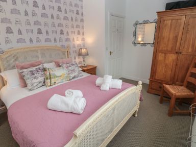 A bedroom with a bed covered with a pink blanket and pillows next to a wooden wardrobe and a chair at The Smithy in Chathill near Seahouses