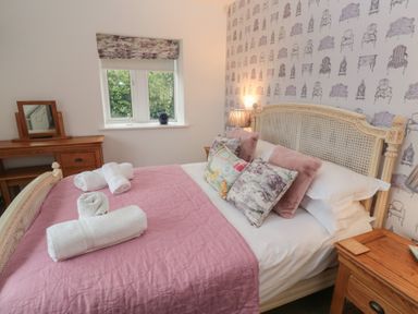 A bedroom with a bed covered in pink bedding and rolled white towels a wooden desk with a mirror and a wooden nightstand at The Smithy in Chathill near Seahouses