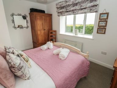 A bedroom with a double bed covered in a pink quilt and white towels on top at The Smithy in Chathill near Seahouses