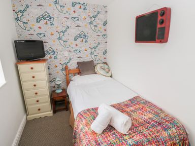 A small bedroom with a single bed a chest of drawers a small table with a lamp and a television mounted on the wall at The Smithy in Chathill near Seahouses