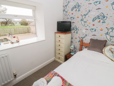 A small bedroom with a single bed a wooden chest of drawers with a television on top a window and nautical themed wallpaper at The Smithy in Chathill near Seahouses