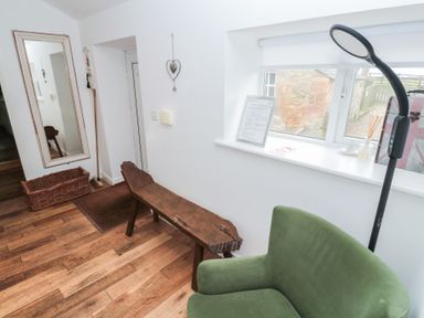A hallway with a wooden bench green armchair floor lamp wicker basket and a tall mirror at The Smithy in Chathill near Seahouses
