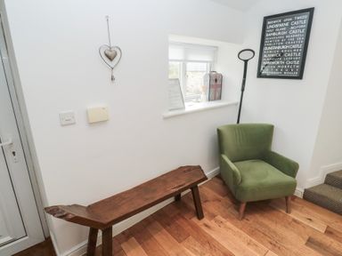 A hallway with a wooden bench a green armchair a window with items on the sill and a framed poster on the wall at The Smithy in Chathill near Seahouses