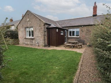 An outdoor area with grass lawn backyard patio wooden picnic table and stone cottage at The Smithy in Chathill near Seahouses