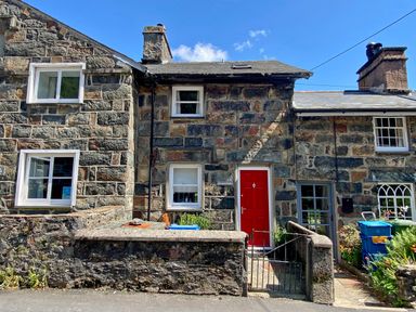 Stone cottages with white window frames and a red door with a small garden and a metal gate at Riverbank Cottage in Beddgelert