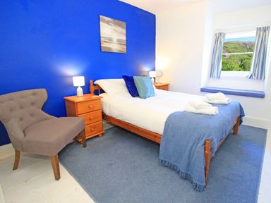 A bedroom with a double bed bedside tables a gray chair and a window seat at Riverbank Cottage in Beddgelert