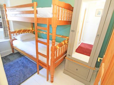 A small bedroom with wooden bunk beds a gray wardrobe with a mirror a blue rug and a window at Riverbank Cottage in Beddgelert
