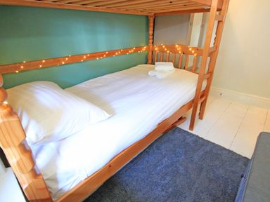 A wooden bunk bed with white bedding and folded towels with string lights on the bed frame at Riverbank Cottage in Beddgelert