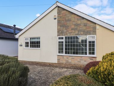 The exterior of a house with two windows a stone and plaster wall and shrubs in the front garden at Samson's Place in Morfa Bychan