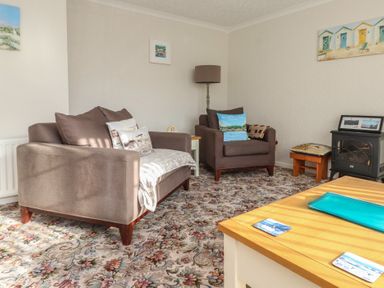A living room with two brown armchairs a floral carpet a wooden table and wall decorations at Samson's Place in Morfa Bychan