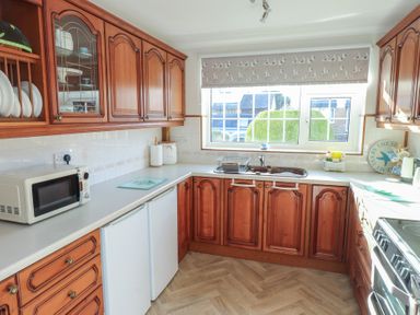 A kitchen with wooden cabinets a microwave a sink and a window with a patterned blind at Samsons Place in Morfa Bychan