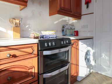 A kitchen with a black oven a washing machine wooden cabinets and kitchen utensils at Samson's Place in Morfa Bychan