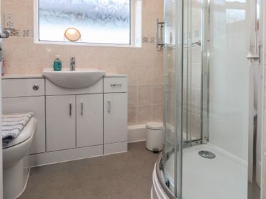 A bathroom with a toilet a sink with cabinet under and a curved glass shower enclosure at Samsons Place Morfa Bychan