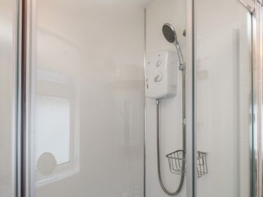 A shower enclosure with a mounted electric shower unit and a handheld showerhead with a metal basket at Samson's Place in Morfa Bychan