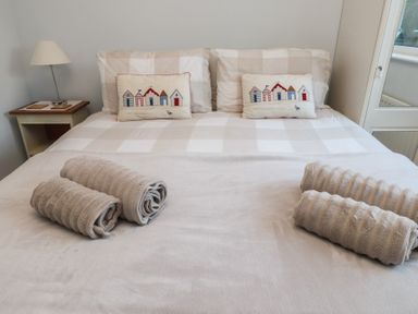 A bed with patterned pillows and rolled towels on a blanket with a bedside table and lamp at Samson's Place in Morfa Bychan