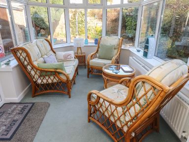 A conservatory with rattan furniture including two armchairs a two-seater sofa a round glass-top coffee table and a side table with a lamp at Samson's Place in Morfa Bychan