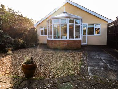 A backyard with a gravel area a potted plant and a conservatory attached to a house at Samson's Place in Morfa Bychan