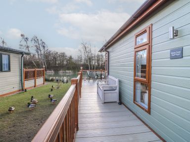 A wooden deck with a bench and table set outside a building near a pond with ducks at Stones Throw in Marston near Barkston