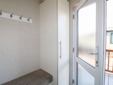 A small entryway with a bench, wall hooks, a tall white cabinet, and a frosted glass door at Stones Throw in Marston near Barkston