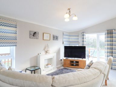 A living room with a large sofa a television on a wooden stand and chevron patterned curtains at Stones Throw Marston near Barkston