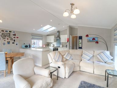 An open living room and kitchen with a beige sofa and armchair a wooden dining table and light blue chairs at Stones Throw in Marston near Barkston